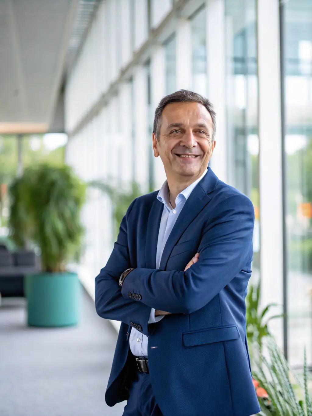 A professional headshot of a business coach smiling confidently, set against a backdrop of a modern office, symbolizing expertise and approachability.